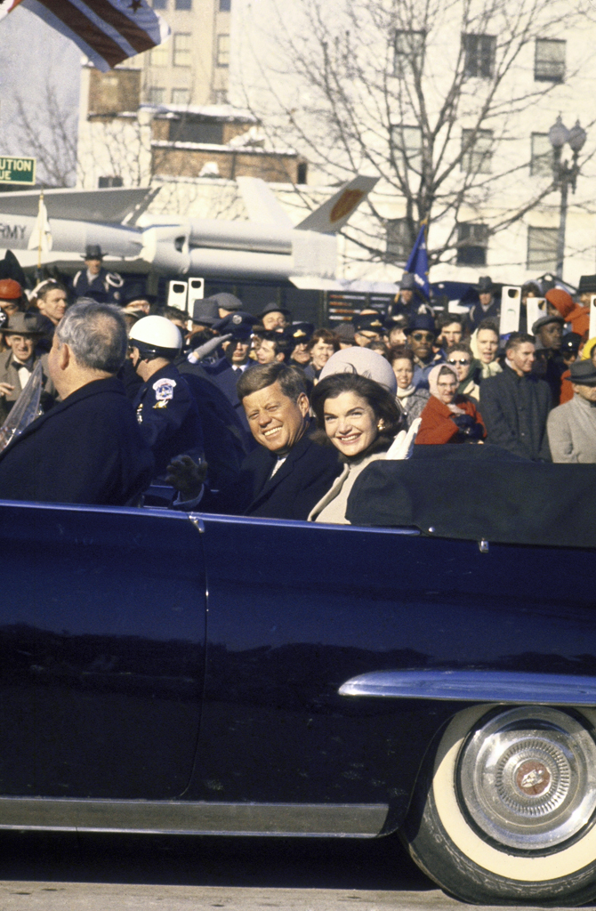 John Kenendy and Jackie Kennedy ride in a blue convertible through a cheering crowd during the Inaugural Parade.