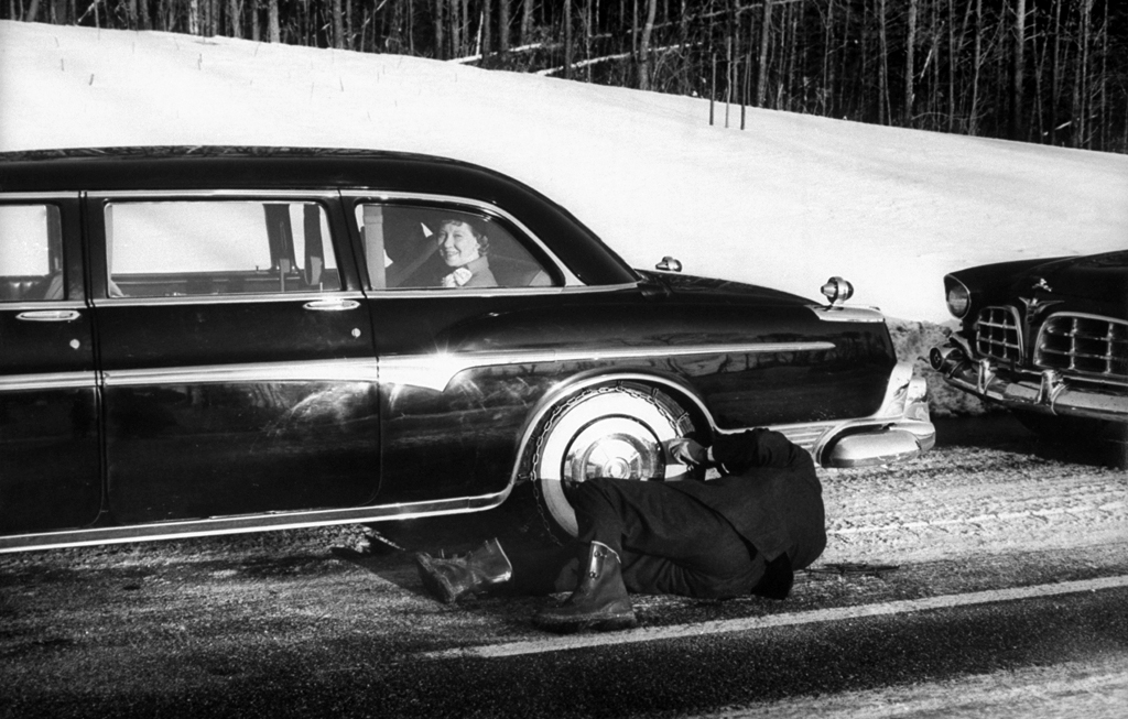 Dwight D. and Mamie Eisenhower wait as their driver takes the snow chains off their limo's tires.