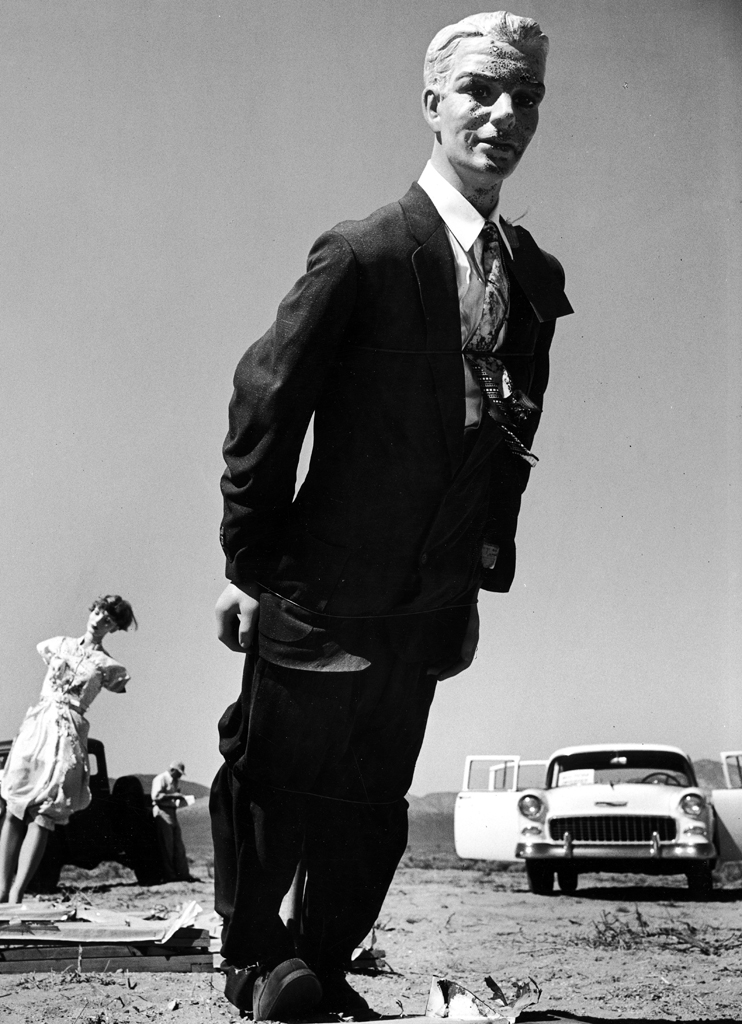 A dummy in a suit stands erect in the foreground with other figures behind to simulate a scene after a test of an atomic bomb.