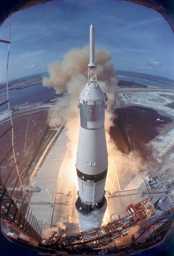 A camera attached above the launch pad captures the Saturn rocket as it lifts off carrying astronauts Neil Armstrong, Buzz Aldrin, and Michael Collins to the moon.
