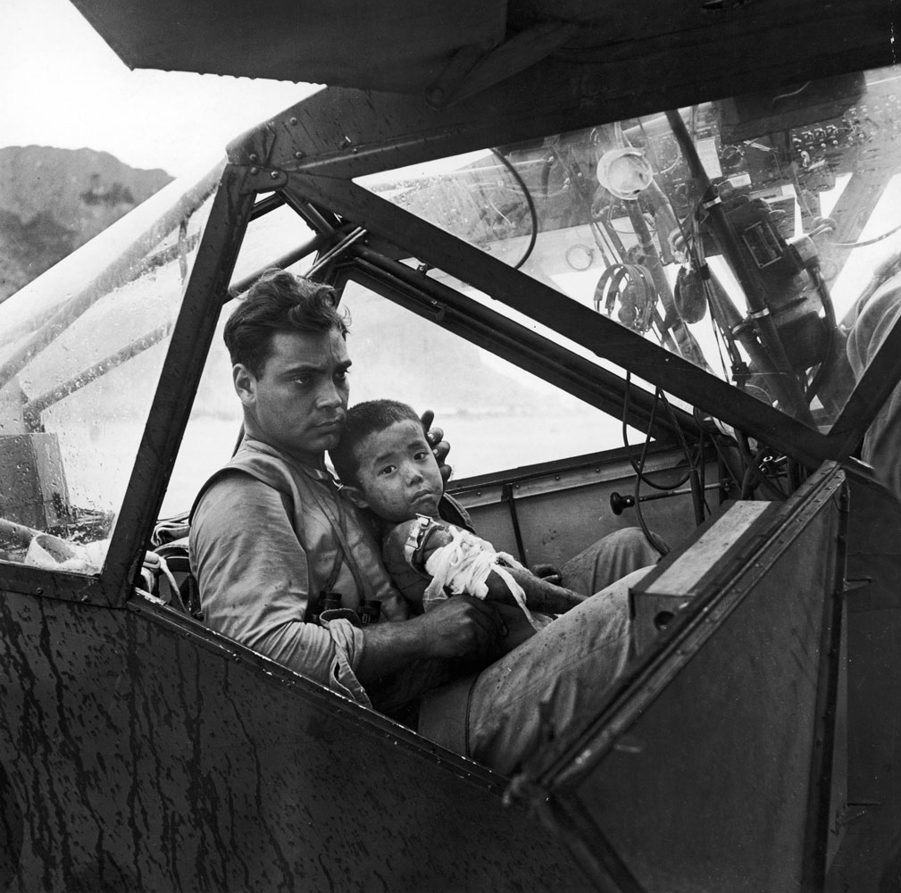 An American soldier holds a wounded Japanese boy in an airplane on Saipan as they await a flight to the nearest field hospital in 1944.