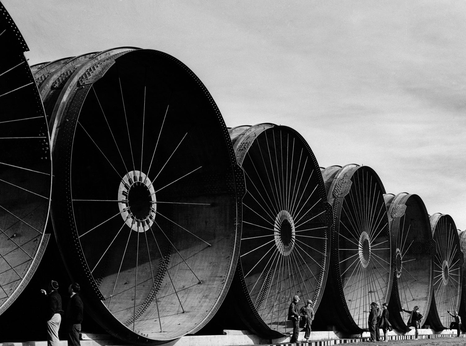 Workmen stand beside giganic pipe segments designed to divert a section on the Missouri River during the construction of Montana's Fort Peck Dam in 1936.