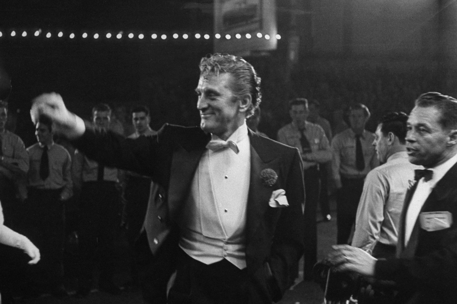 Kirk Douglas, elegant in white tie, smiles and waves as he enters the RKO Pantages Theater in 1954.