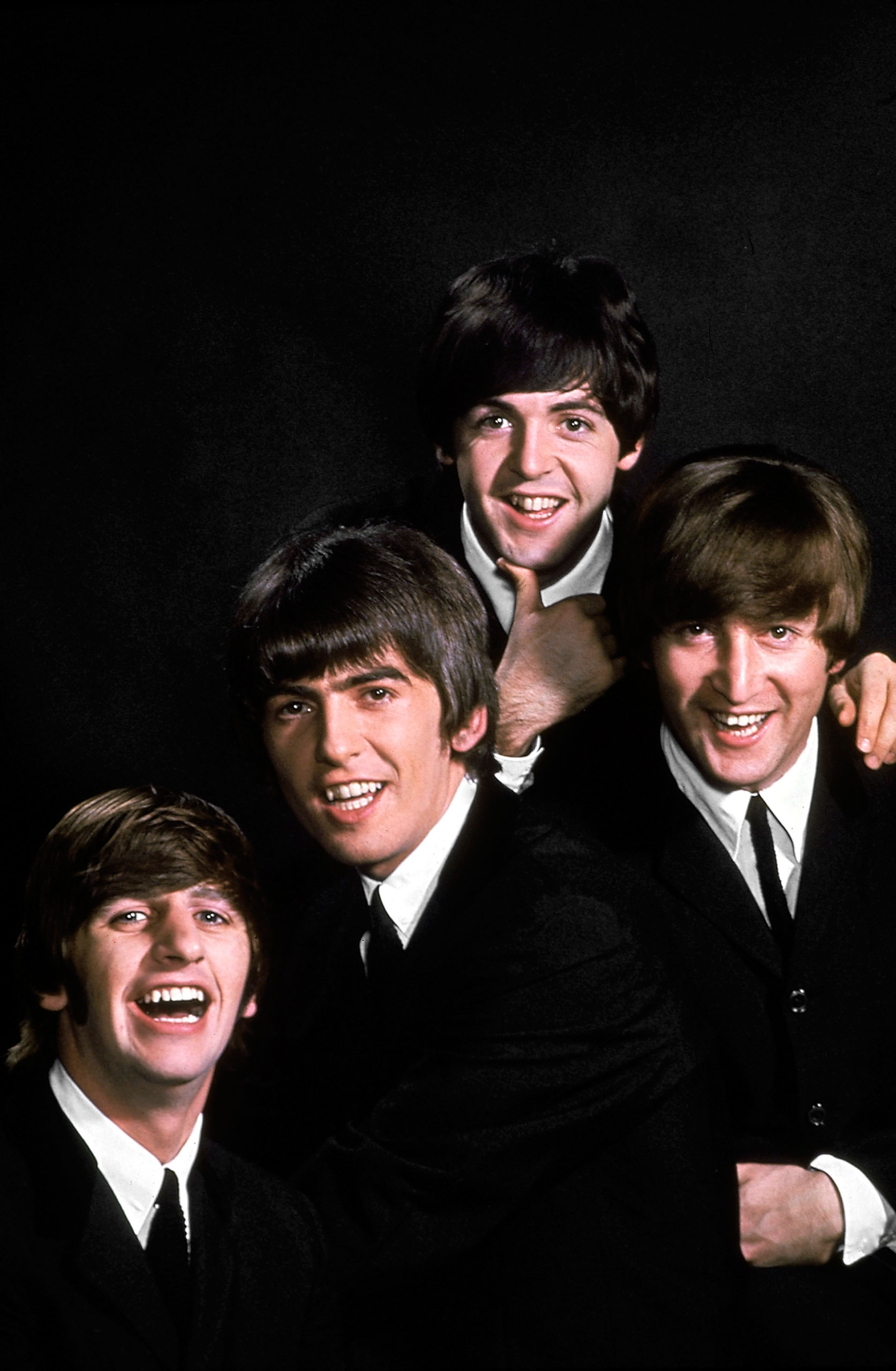 John Lennon, Paul McCartney, George Harrison, and Ringo Starr pose in a portrait on a black backdrop in January 1964