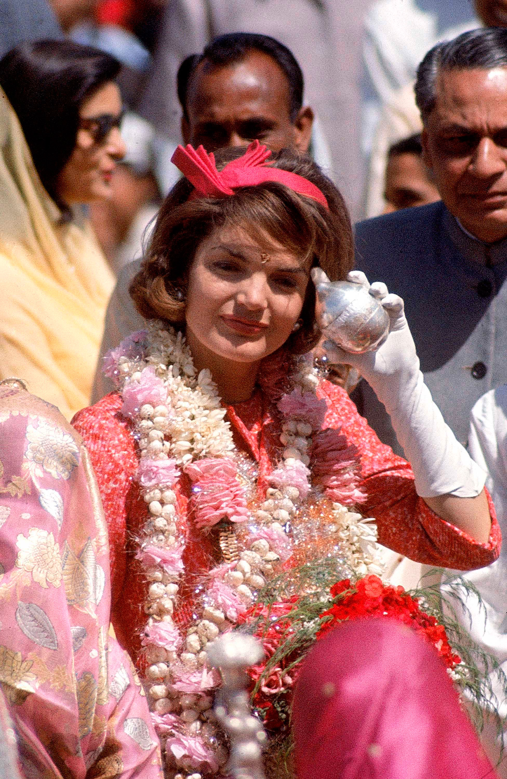 In a sea of Indian saris, Mrs. Kennedy and Rajasthan's governor move through Jaipur airport. On her forehead is the Rajasthani mark of luck and respect, the tika. Her silver-encased coconut also honors the occasion