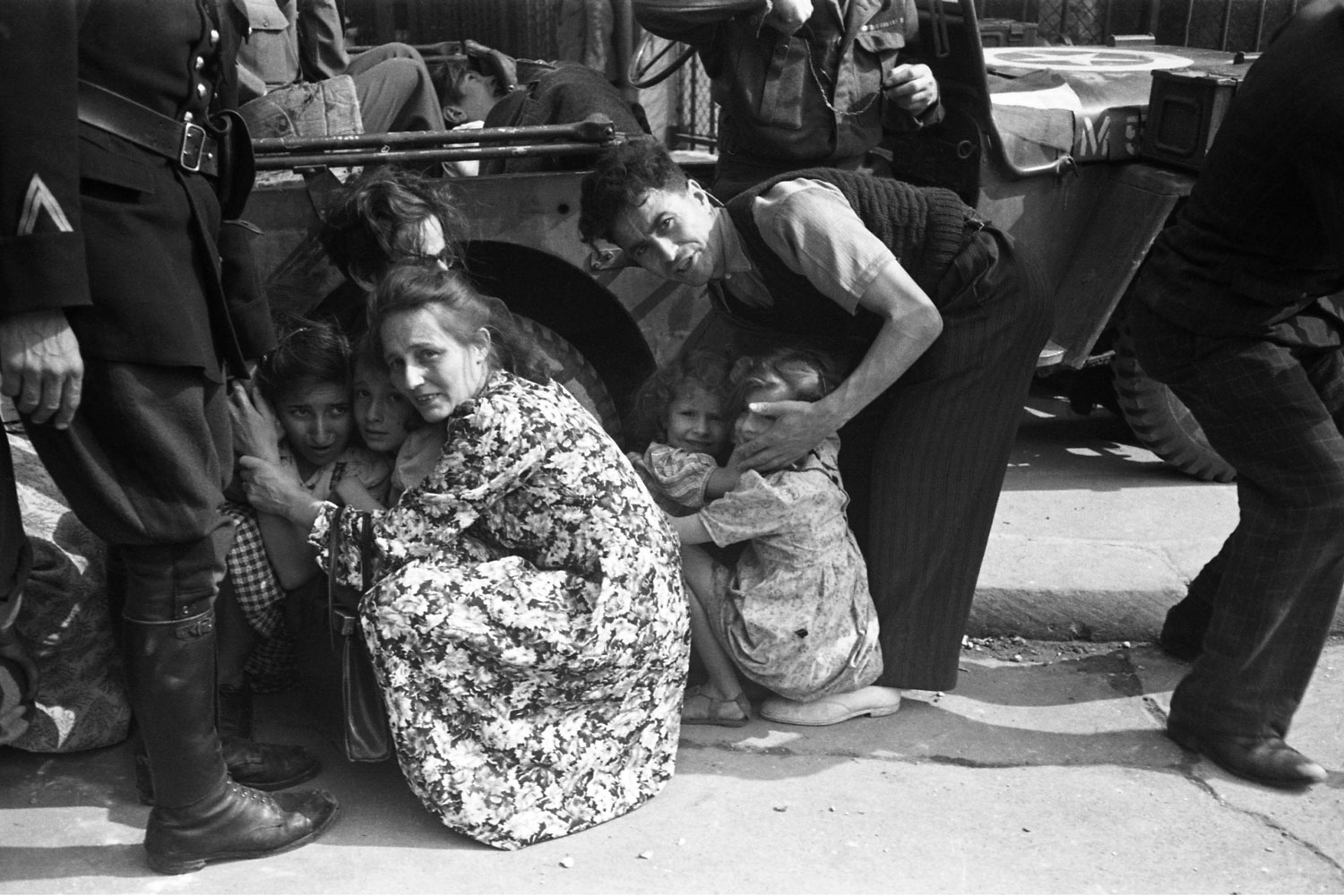 A family seeks safety beside a Jeep as French Resistance fighters and Free French troops try to take out a German sniper during the Liberation of Paris on August 25, 1944.