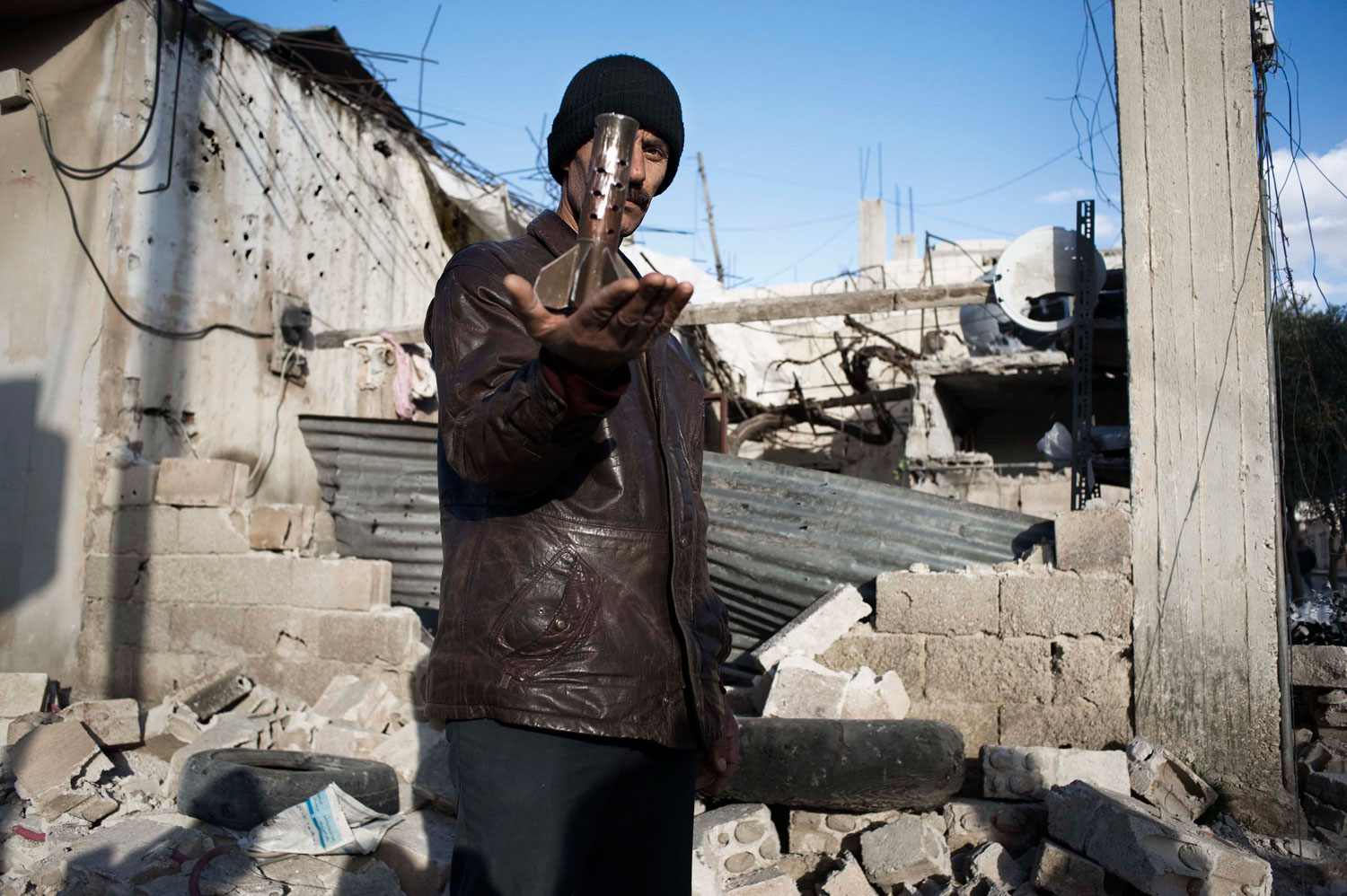 Feb. 9, 2012. A man displays part of a mortar lauched by the Syrian Army that destroyed the house behind him, in al-Qsair.
