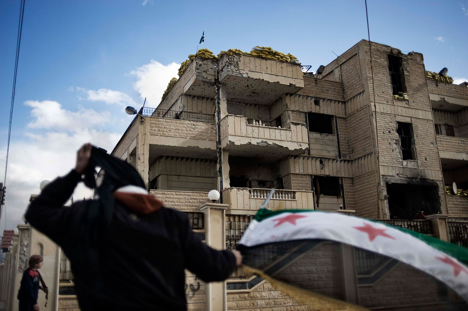 Feb. 10, 2012. A man waves the old Syrian flag in front of the former police station in al-Qsair.