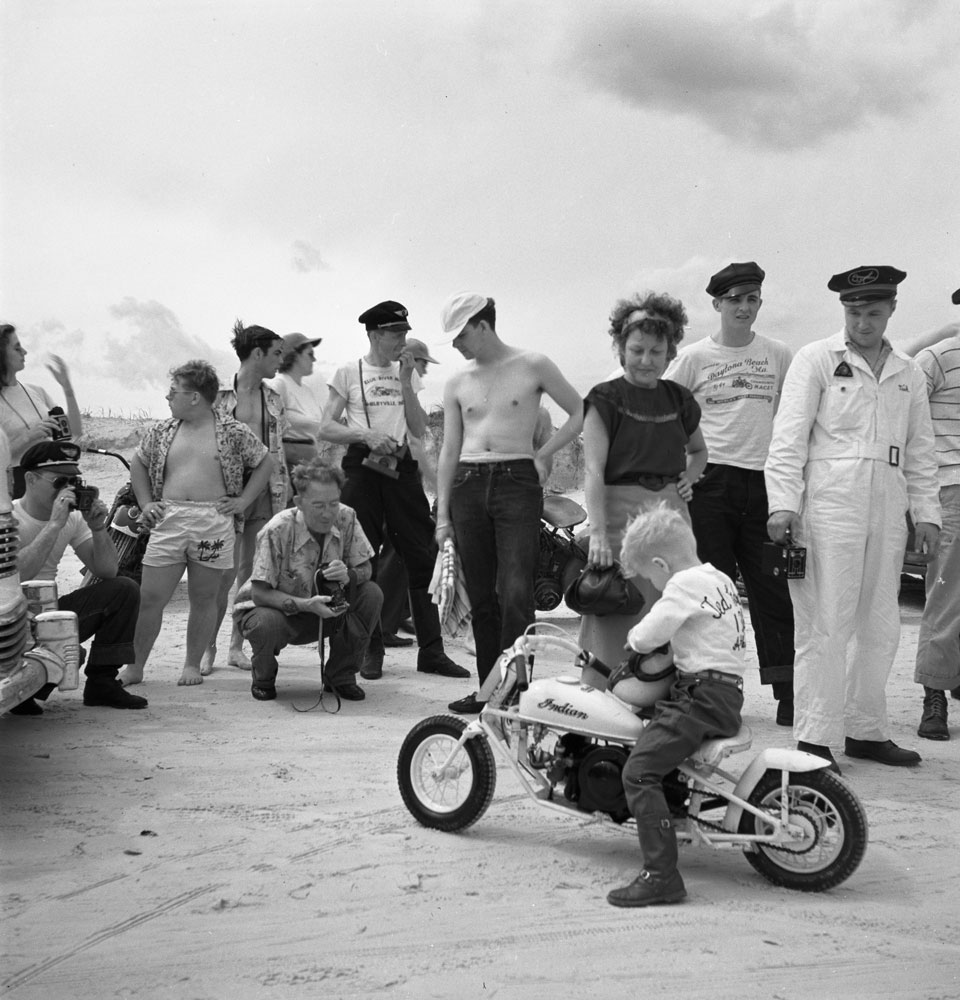 A young boy adjusts his helmet while seated astride a miniature Indian motorbike, Daytona Beach, Florida, March 1948.
