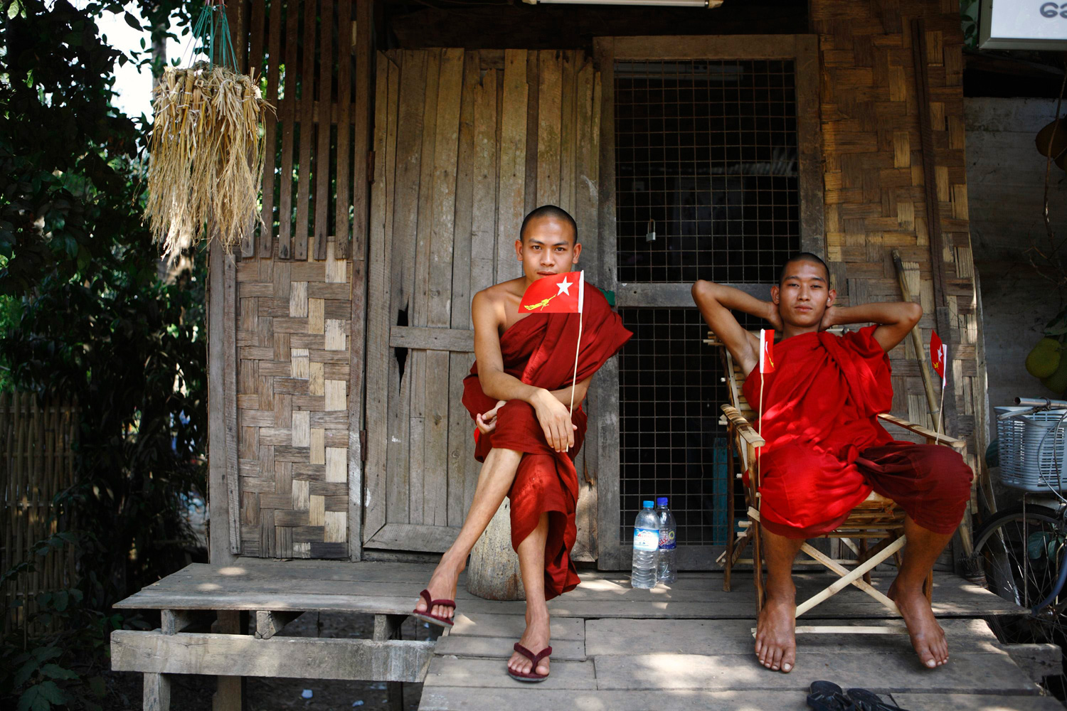 March 28, 2012. Buddhist monks hold the party flag as they rest outside a house during the election campaign for the NLD party in Yangon, Myanmar.