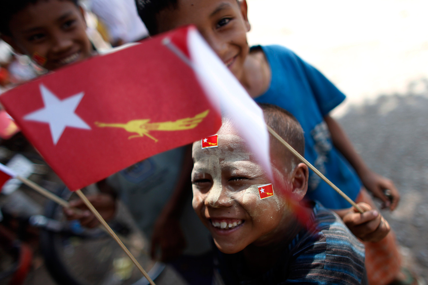 March 28, 2012. Children, holding flags of the National League for Democracy, react to the camera during a campaign rally for the April 1 by-election on Eight Mile Junction in Yangon, Myanmar.