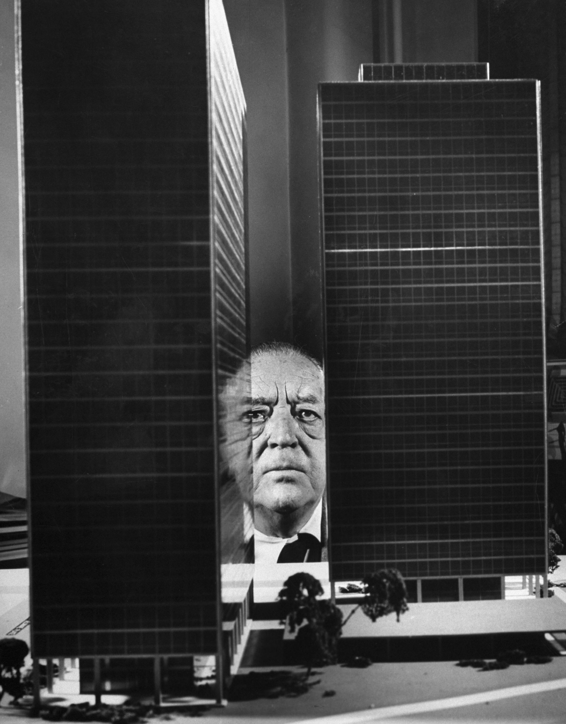 Architect Ludwig Mies van der Rohe peers between two large models of ultra-modern apartment buildings he designed for Chicago's Lake Shore Drive, 1956.
