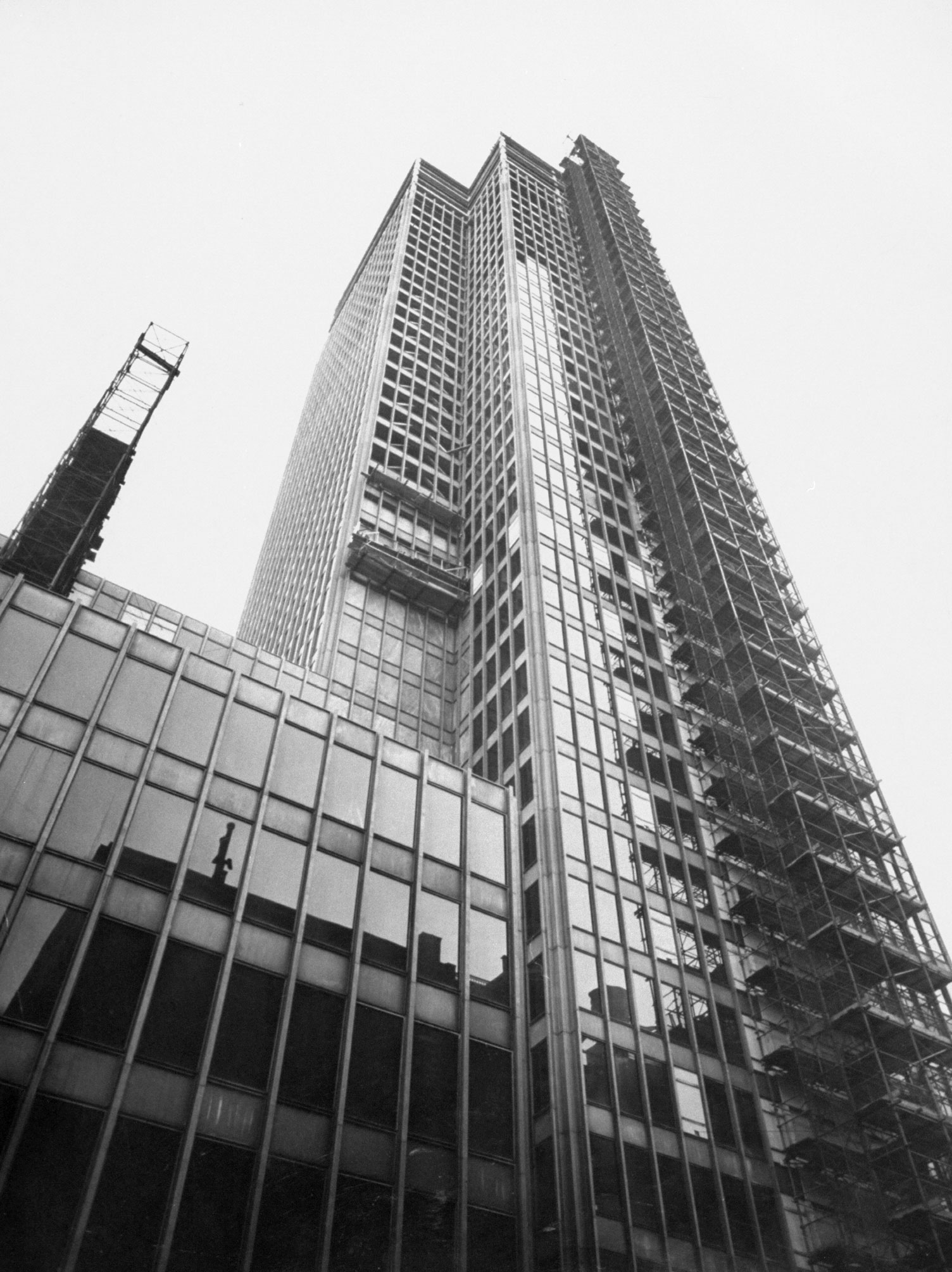 Mies' Manhattan Tower, the 38-story Seagram Building under construction on Park Avenue, is flanked by elevator shafts for lifting building materials to top. In rare switch for Mies, indented area at left has marble walls, not glass.