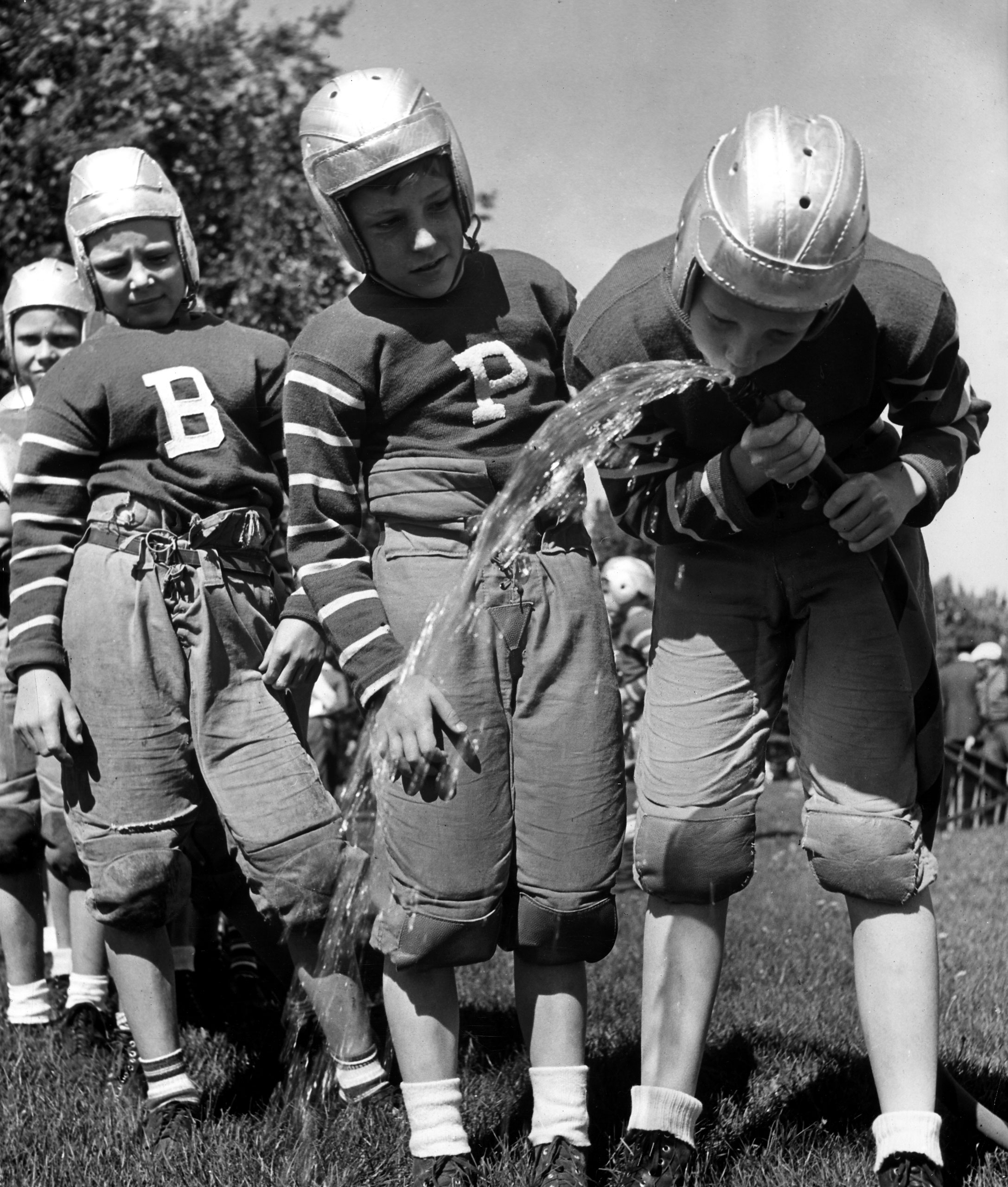 Thirsty young football players drink water from a garden hose in Denver, Colorado, in 1939.