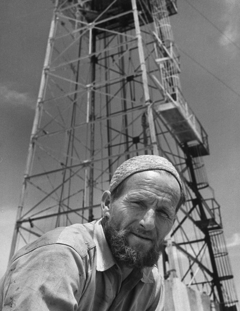 Jack Stovall, native of Texas, is an assistant driller. He has grown and Arabian-type beard, is wearing an Arabian-type cap. Many Americans become proficient at speaking Arabic.