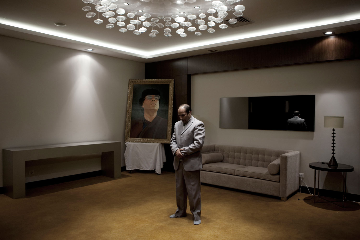 March 14, 2011. A man performs his evening prayers next to a portrait of Libyan leader Muammar Gaddafi, in the lobby of a hotel in which a press conference by tribal leaders was taking place in Tripoli.