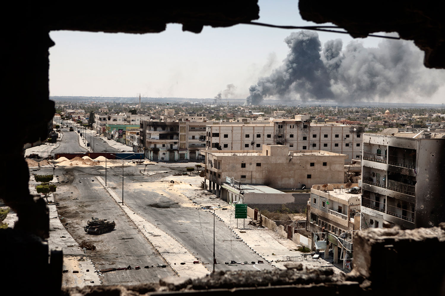 April 29, 2011. Smoke billows from a shoe factory on the frontline near the airport, with the bombed out remains of buildings on Tripoli Street in the foreground, in Misurata.