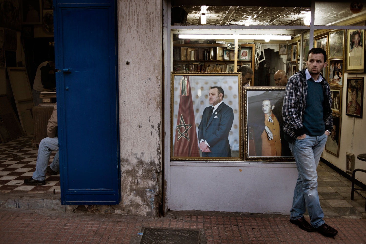 March 2012. A Moroccan man stands next to the portraits of King Mohammed in the old souk in Rabat, Morocco. The monarch is widely accepted as “commander of the faithful,” which makes any direct criticism of him close to sacrilegious. But there is widespread dissatisfaction over corruption among his close aides.