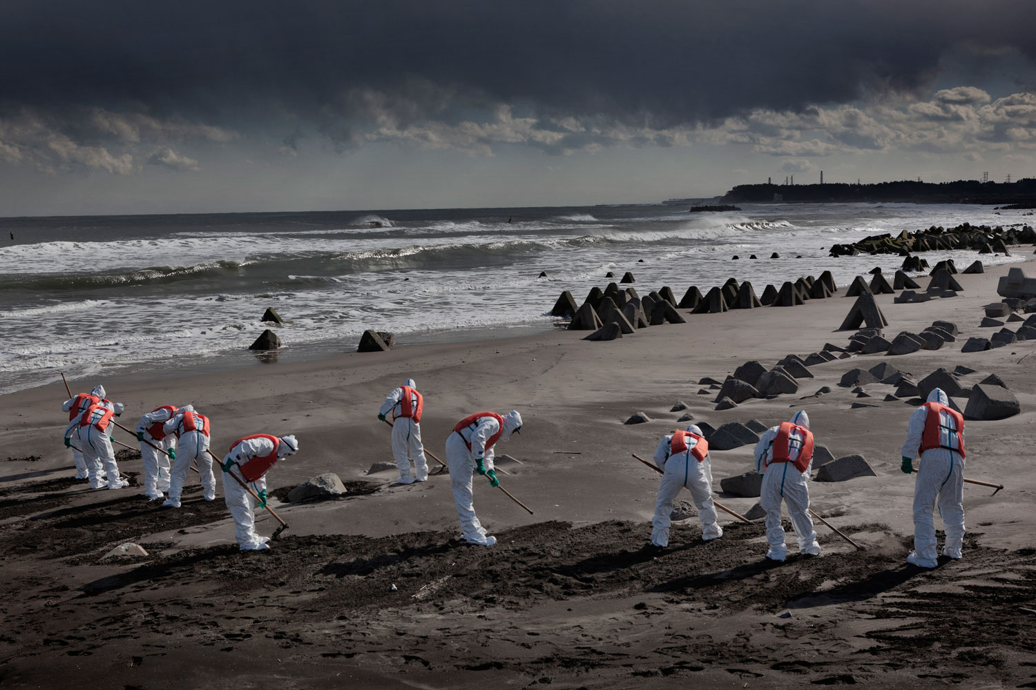 Feb. 27, 2012. Namie, Japan. Police from Futaba District Police Station, which is inside the exclusion zone, search for the dead and still-missing along the ocean front near the power plant, the stacks of which can be seen in the far distance.