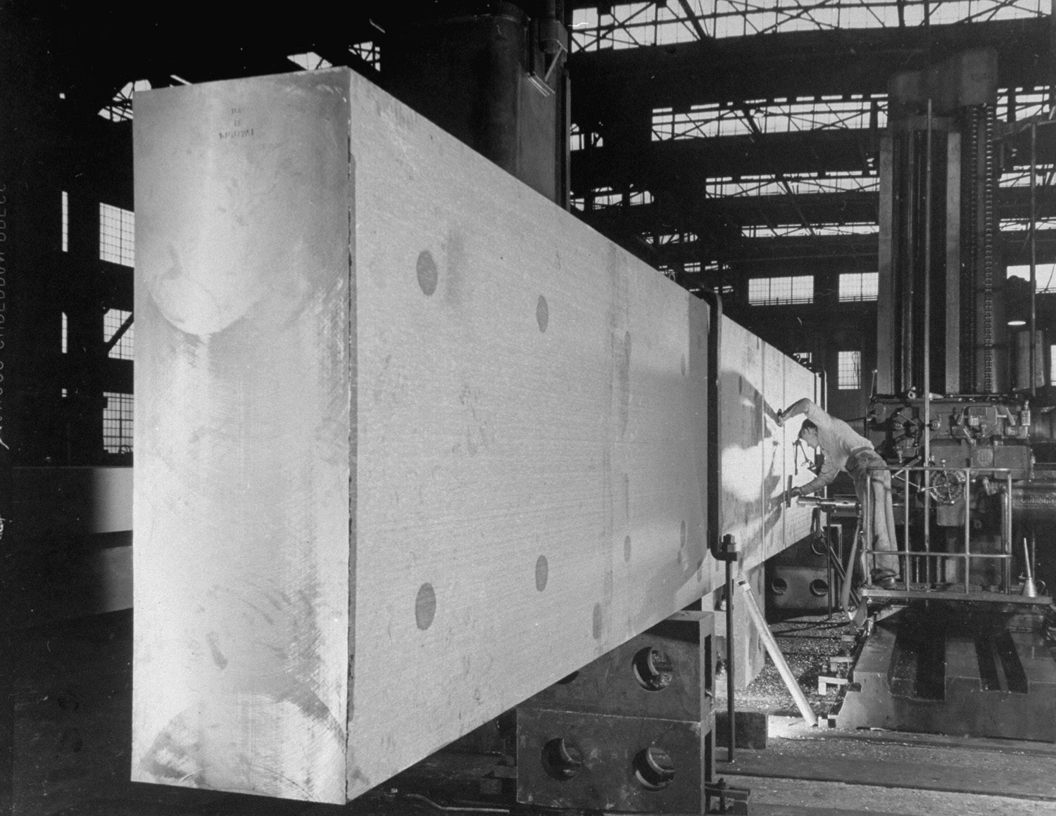 A steel worker in Bethlehem, Penn., drills holes in a massive, forged beam; the beam will form part of the framework of a large cyclotron magnet.