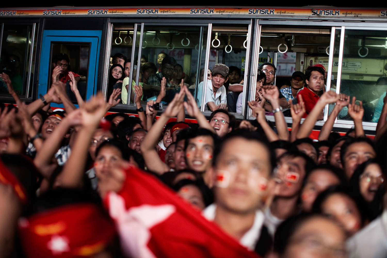 April 1, 2012. Passengers on a bus watch as supporters of Aung San Suu Kyi and her party, the National League for Democracy, gather outside the party's headquarters in Yangon, Myanmar.