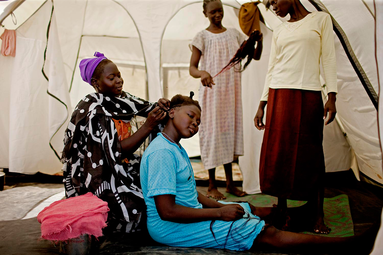 Nuban girls braid each other's hair inside their tent in the Paryang refugee camp.