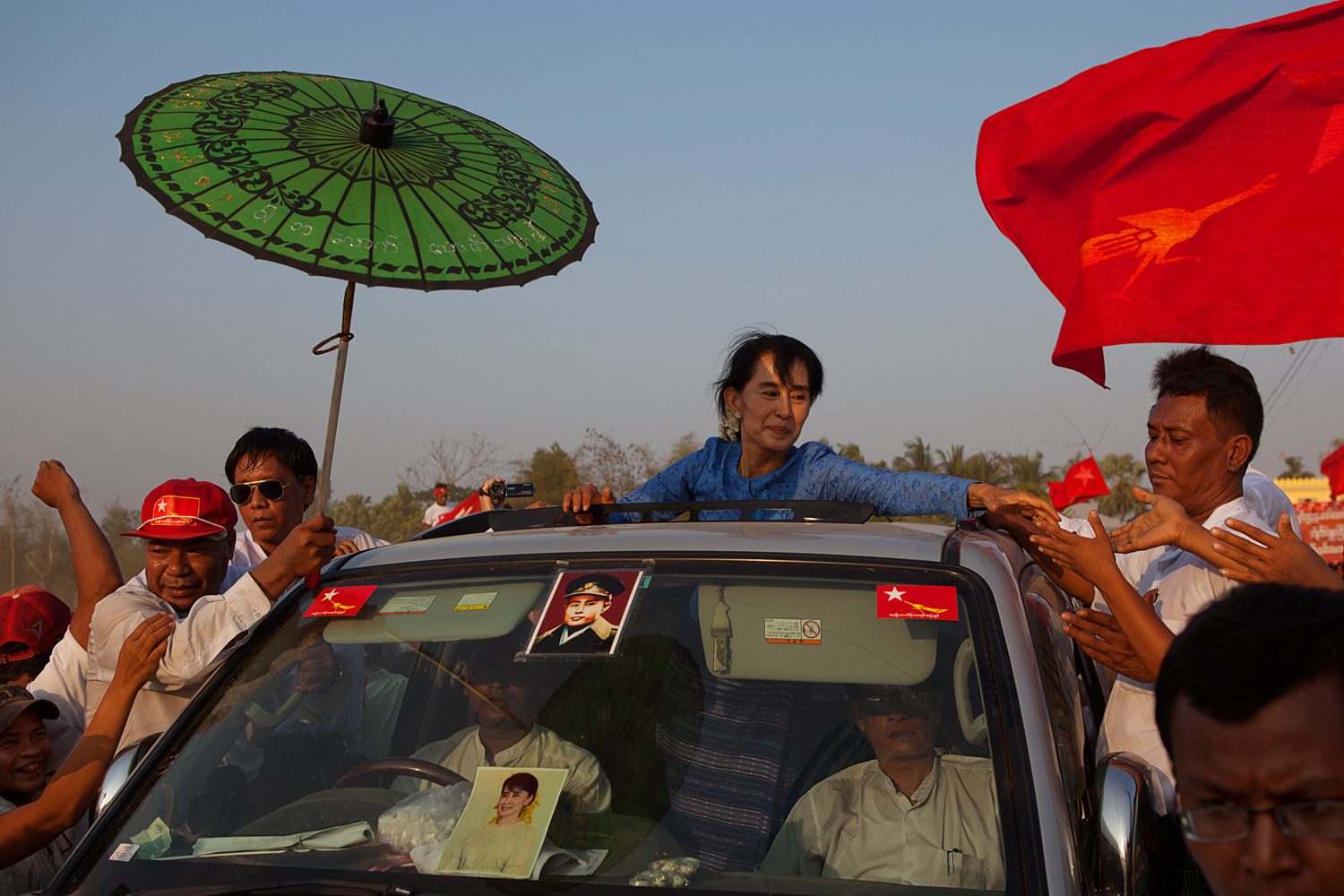 March 22, 2012. Aung San Suu Kyi departs from a campaign rally in Kawhmu, the district from which she ran for a seat in Parliament. She emerges from the sun roof to shake hands with thousands of well-wishers who lined the road. A staff member holds a parasol to protect her from the sun.
