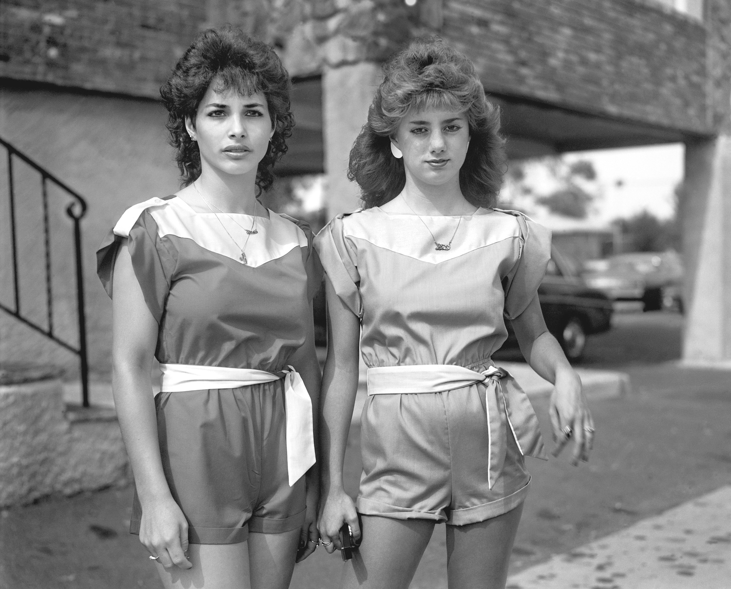 Two young women in matching outfits in front of an open air garage.