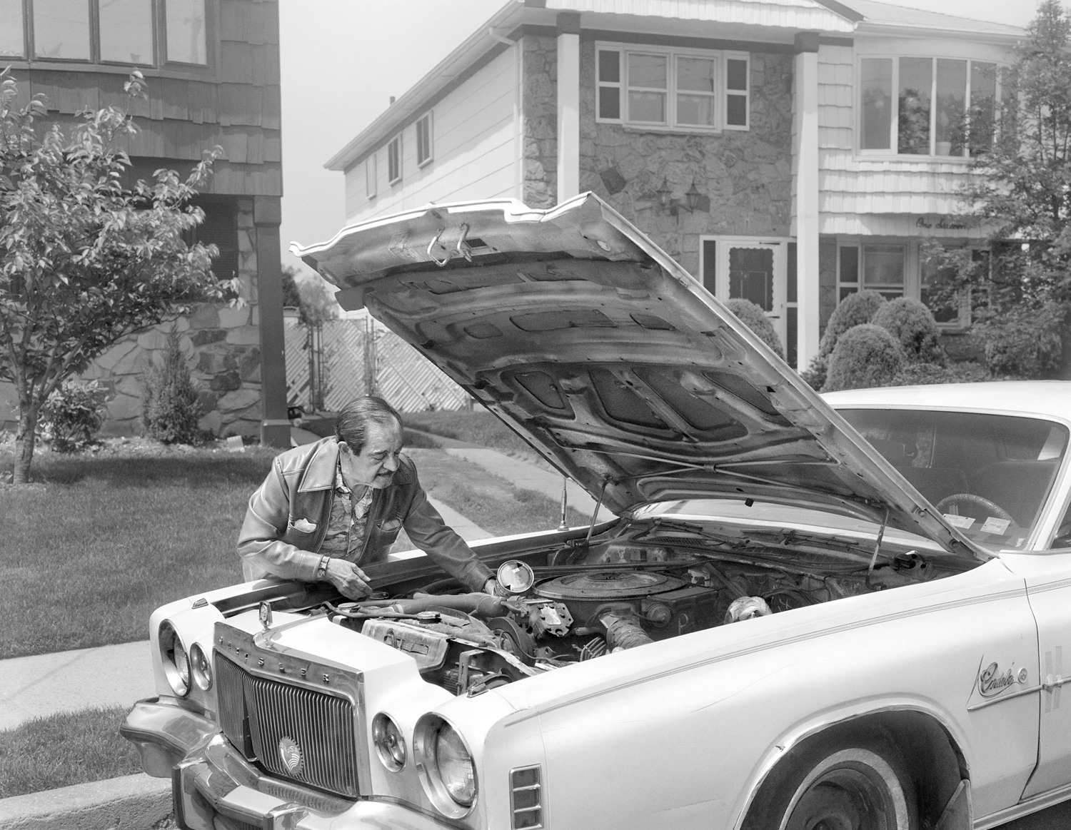Man putting oil in his Chrysler Cordoba in front of his home.