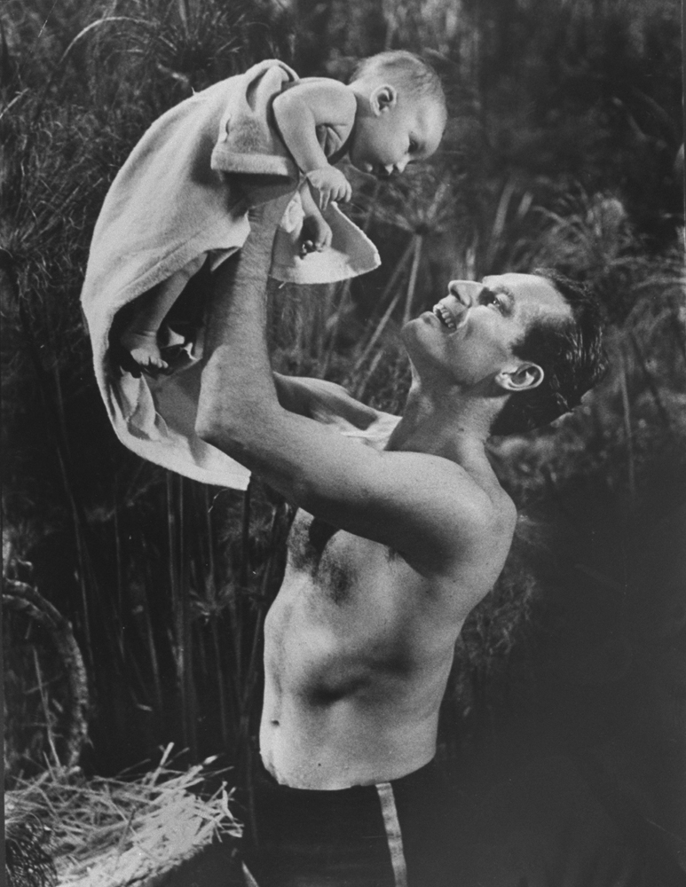 Actor Charlton Heston lifting two-month-old son Fraser, who is portraying the baby Moses, into the air during filming of C.B. DeMille's "The Ten Commandments."