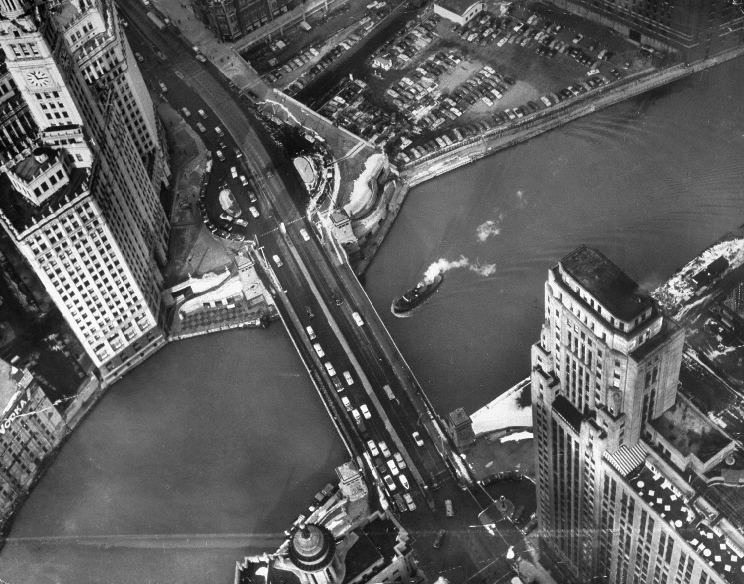 Caption from LIFE.  Chicago's famous Wrigley Building looks like candy castle from a helicopter above spire. Building is split in two parts and a railroad track runs between them. Behind them is Chicago River, with Michigan Avenue bridge.