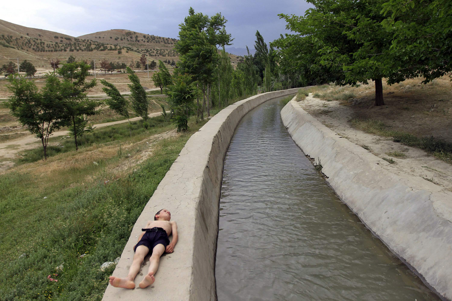 A boy lies on the side of a stream in Kabul