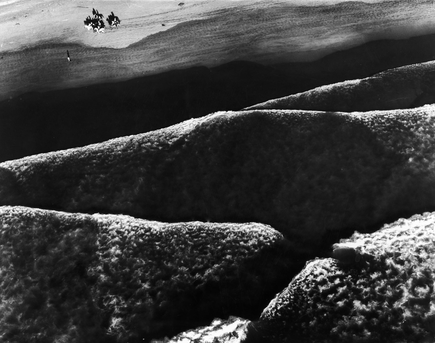 Caption from LIFE.  Beach riders guide their horses along the shore at high tide at Ocean Beach, near Fort Funston, Calif., as the long, low Pacific rollers make mountain like patterns of the surf.