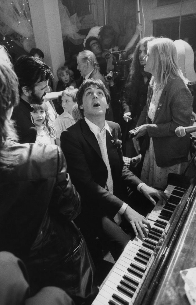 Former Beatle Paul McCartney (center) provides musical entertainment at the wedding reception of ex-Beatles drummer Ringo Starr (left) and Barbara Bach (not pictured). Starr's daughter Lee Starkey stands next to him; also singing along is McCartney's wife Linda (right). At the London club Rags, April 1981.