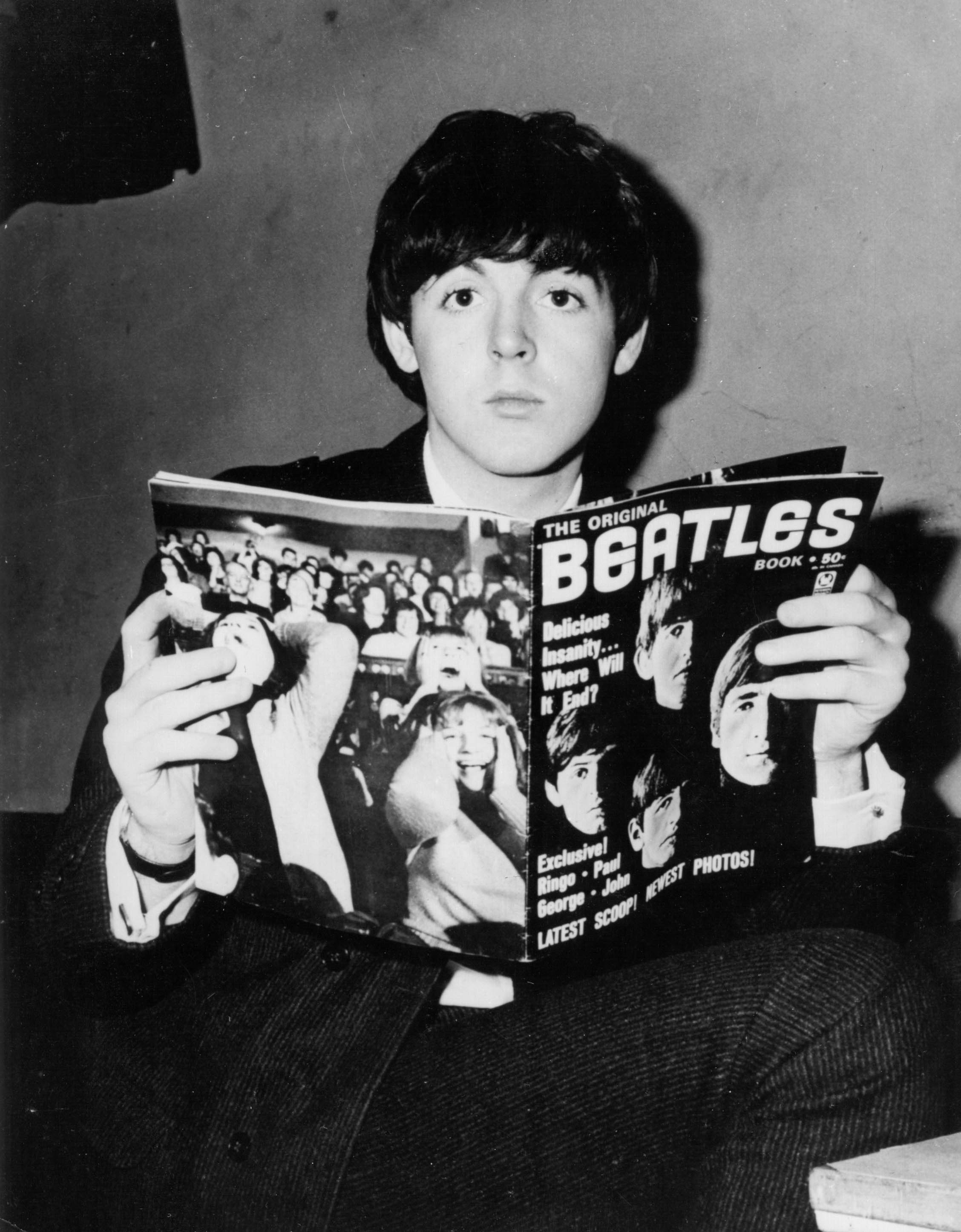 Paul McCartney poses for a portrait holding a Beatles fanzine which depicts 'Beatlemania' on the back cover, 1964.