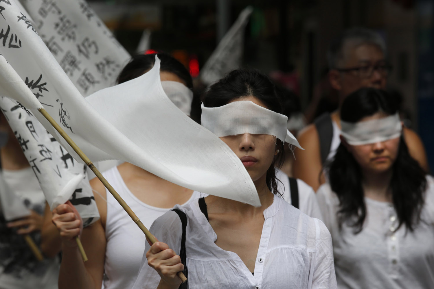 June 10, 2012. Protesters wear white dresses and cover eyes with white clothes to mourn for the death of Chinese labor activist Li Wangyang during a protest march in Hong Kong.