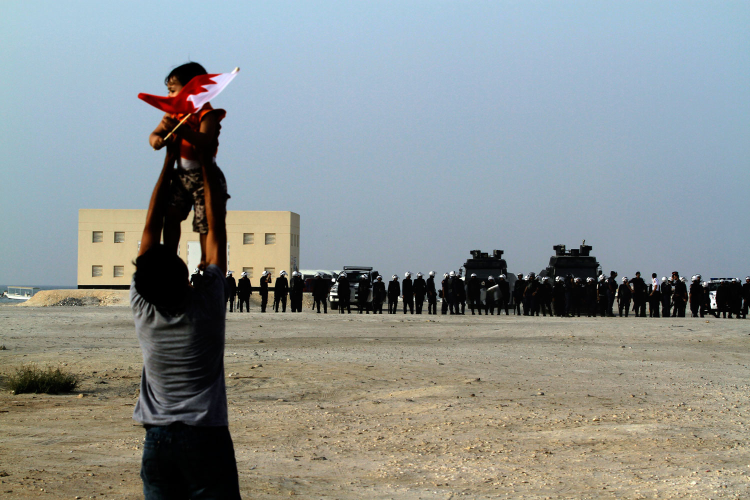 A Bahraini anti-government protester holds up a child carrying a national flag