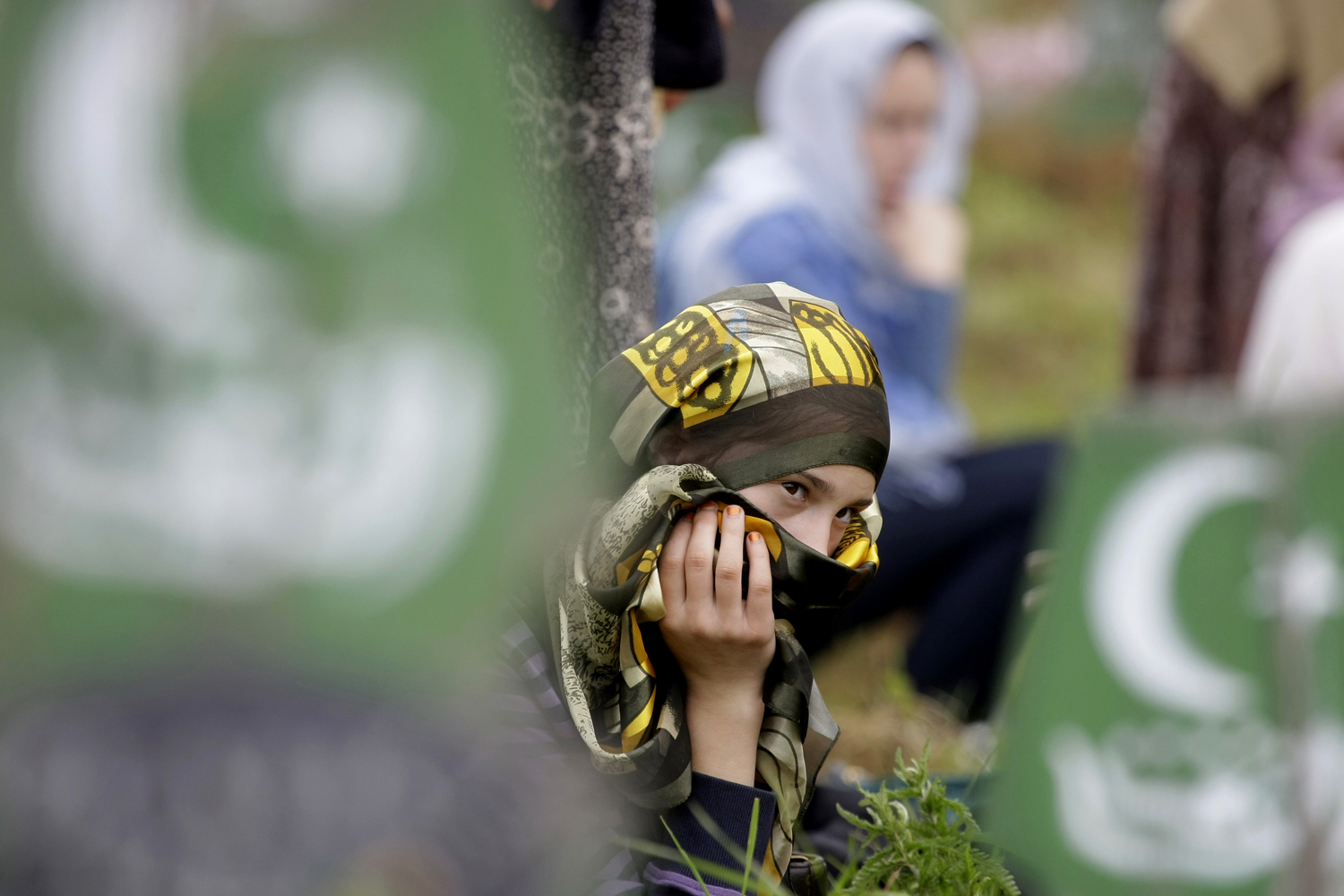 June 2, 2012. A Bosnian Muslim girl sits amidst wooden grave markers during a mass funeral in the eastern Bosnian town of Kalesija. Thousands have gathered in Kalesija to bury the 32 Muslim Bosniaks, killed at the start of the country's 1992-95 war, whose remains were discovered in numerous mass graves and identified through DNA analysis.