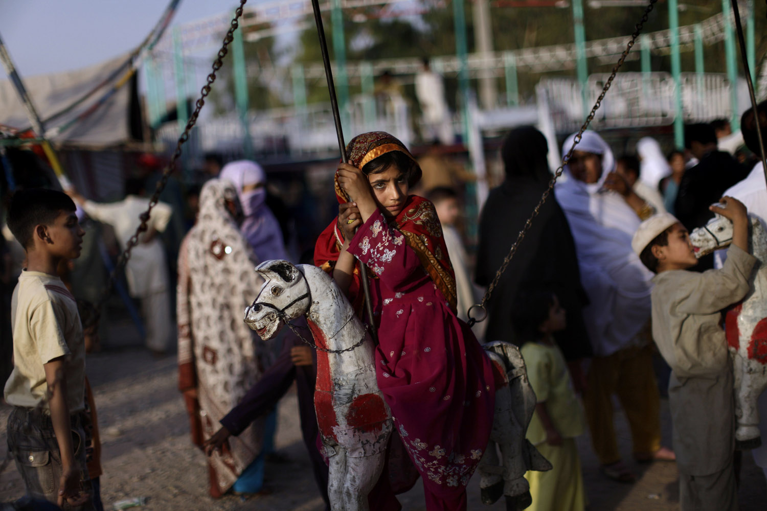 A Pakistani girl sits on a merry-go-round, hoping to have a free ride, at an entertainment park in Rawalpindi, Pakistan