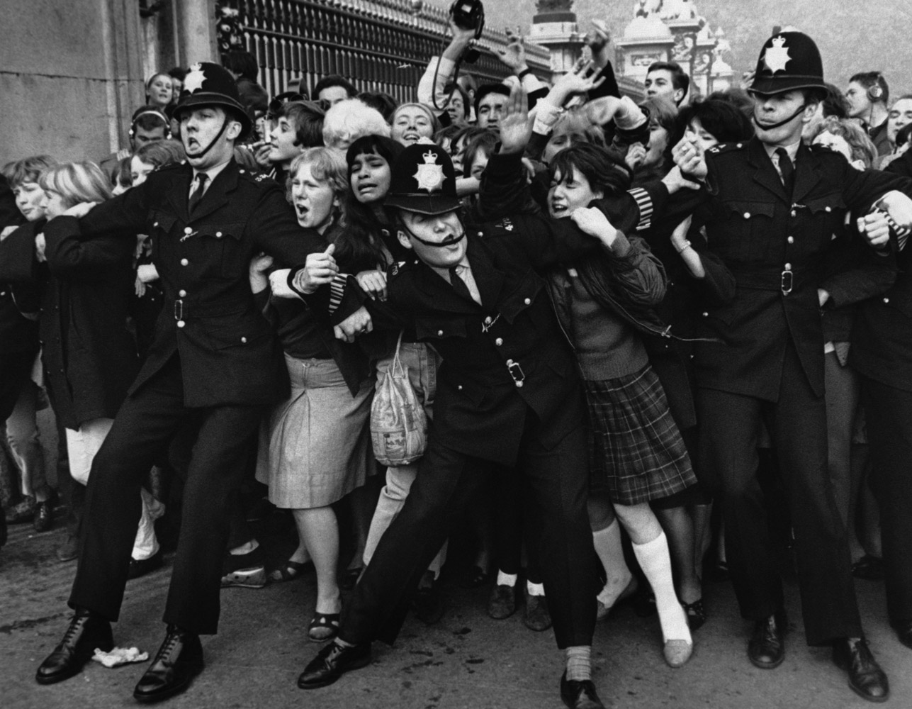 Policemen struggle to restrain young Beatles fans outside Buckingham Palace as The Beatles receive their MBEs (Member of the British Empire) in October 1965.  London, England.  John Lennon later returned his MBE in September 1969, in protest against British politics.