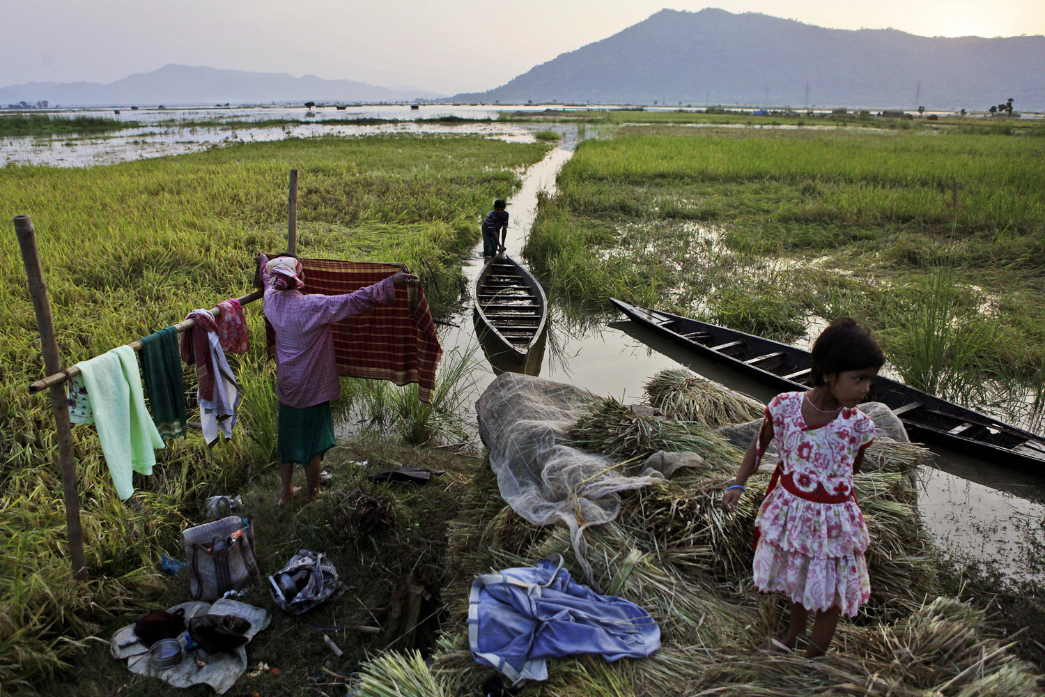 June 8, 2012. A man pushes a boat as a woman dries clothes in a paddy field flooded by rain water in Pobitora, India.