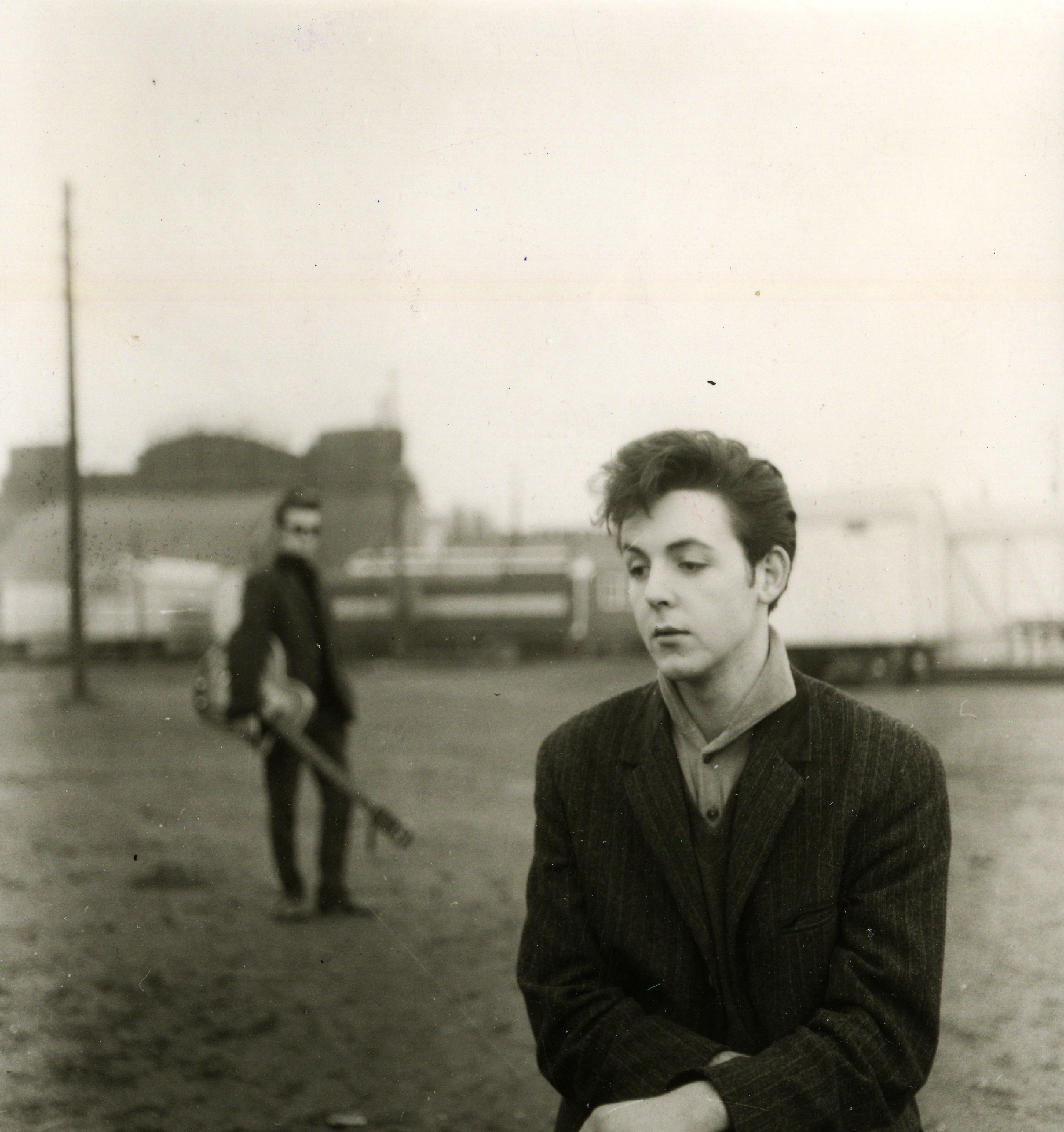 Portrait of Paul McCartney taken at the Hamburg fairgrounds with Stuart Sutcliffe in the background. Hamburg, Germany,1960.
