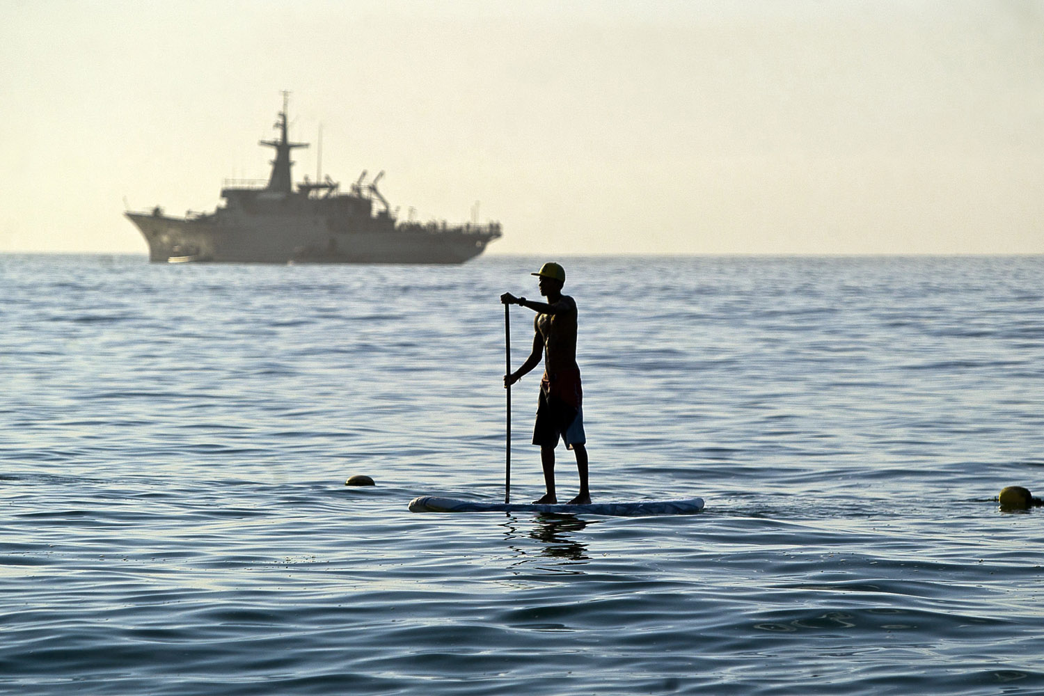 June 8, 2012. A man stand-up paddle surfs as a Mexican navy ship patrols the bay waters in San Jose del Cabo in Mexico's Baja Peninsula. Security has been beefed up in preparation for the upcoming G-20 that will be held in Los Cabos June 18-19.