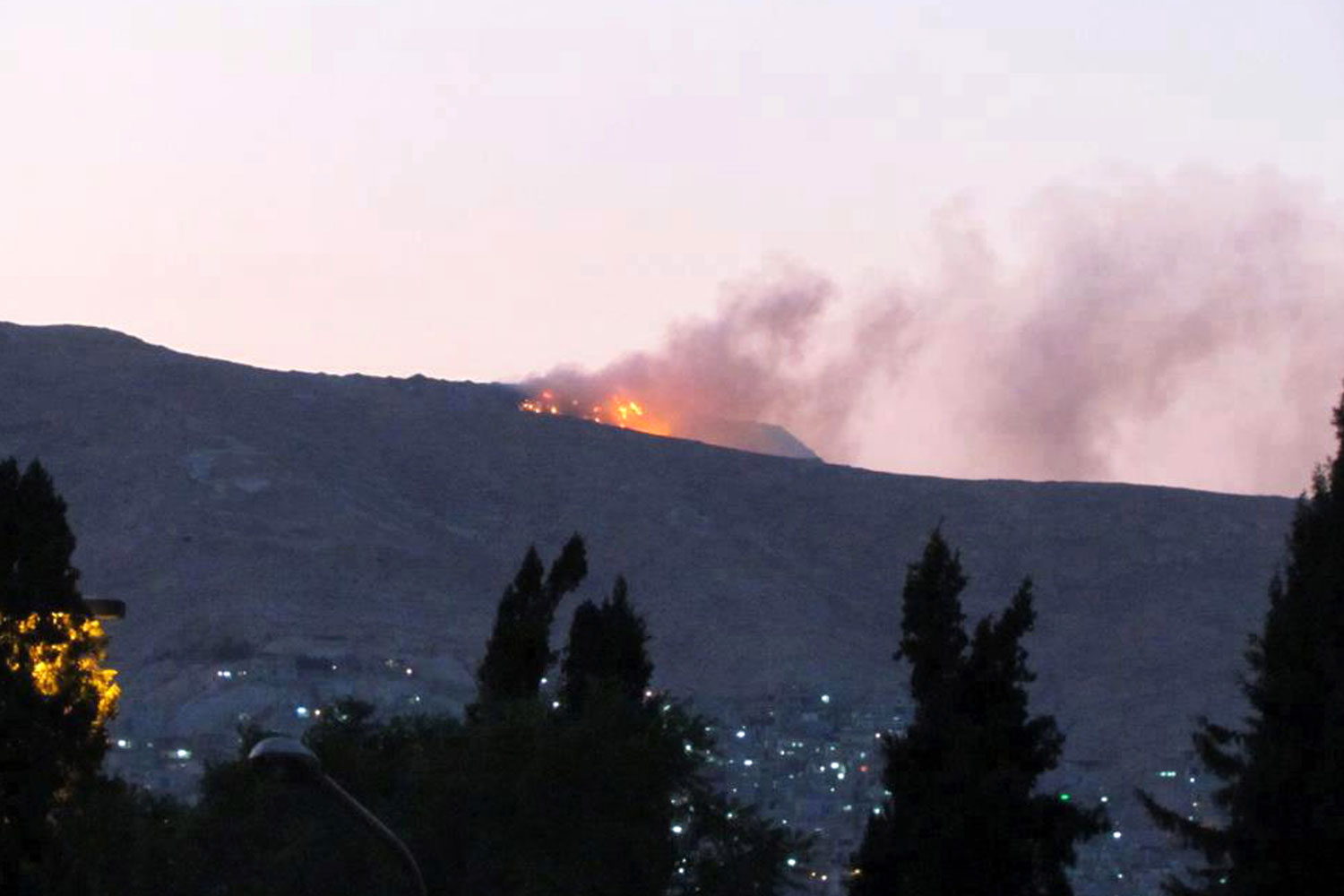 July 19, 2012. A fire is seen in the army barracks on Mount Qassioun, above the presidential palace in Damascus as rebels seized control of all of Syria's border crossings with Iraq.