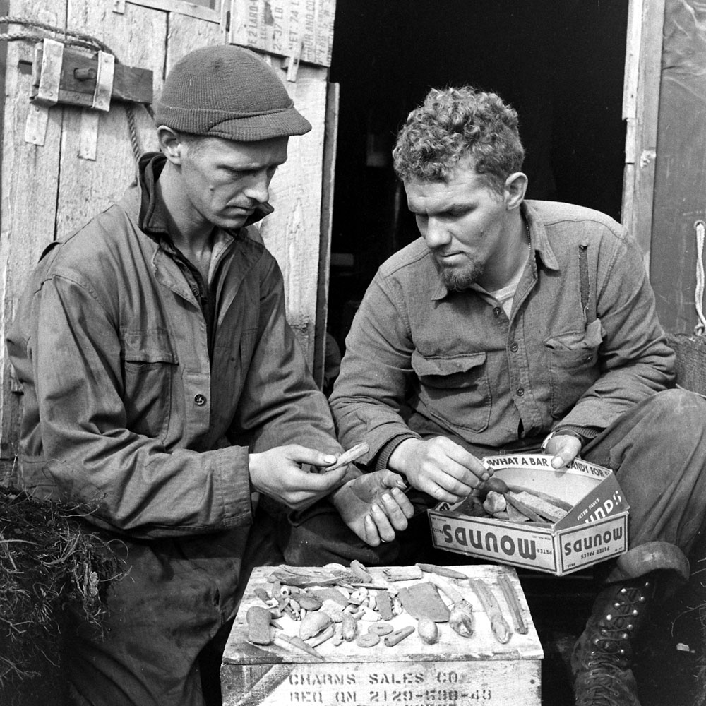 American troops study stone and bone implements and other objects recovered from an earlier settlement, Aleutian Islands Campaign, Alaska, 1943.