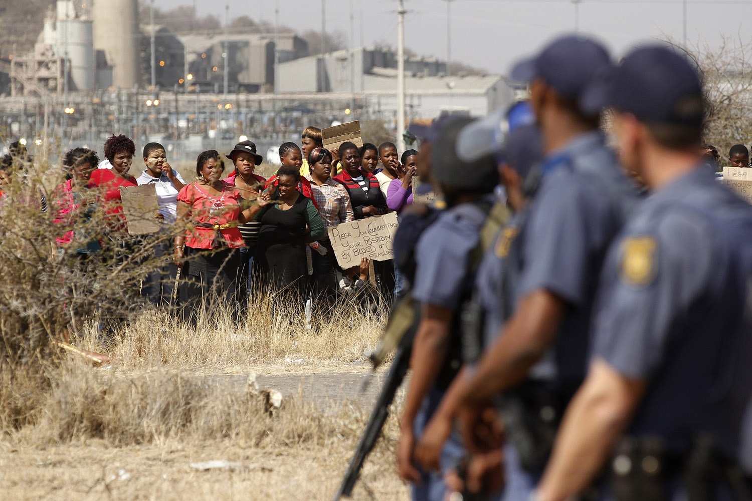Aug. 17, 2012. Police look on as women carry placards in protest against the killing of miners by the South African police outside a South African mine in Rustenburg, 100 km (62 miles) northwest of Johannesburg.