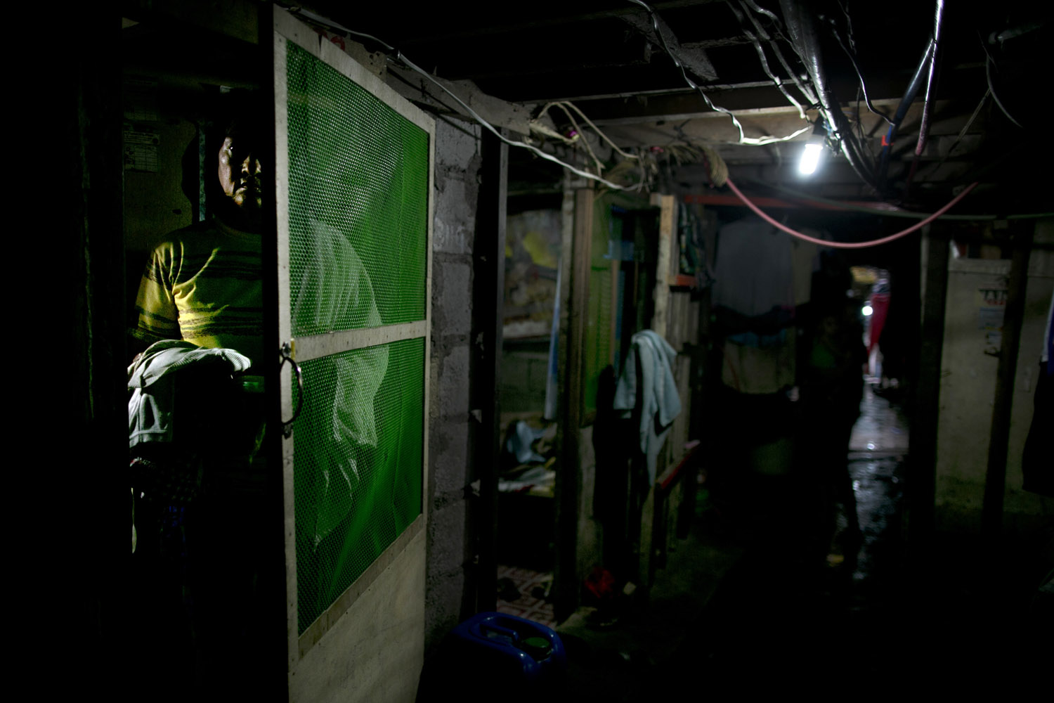 Aug. 21, 2012. A man stands next to the door of his room under a bridge in Manila. Families cram into small rooms under a bridge so they can live for free.