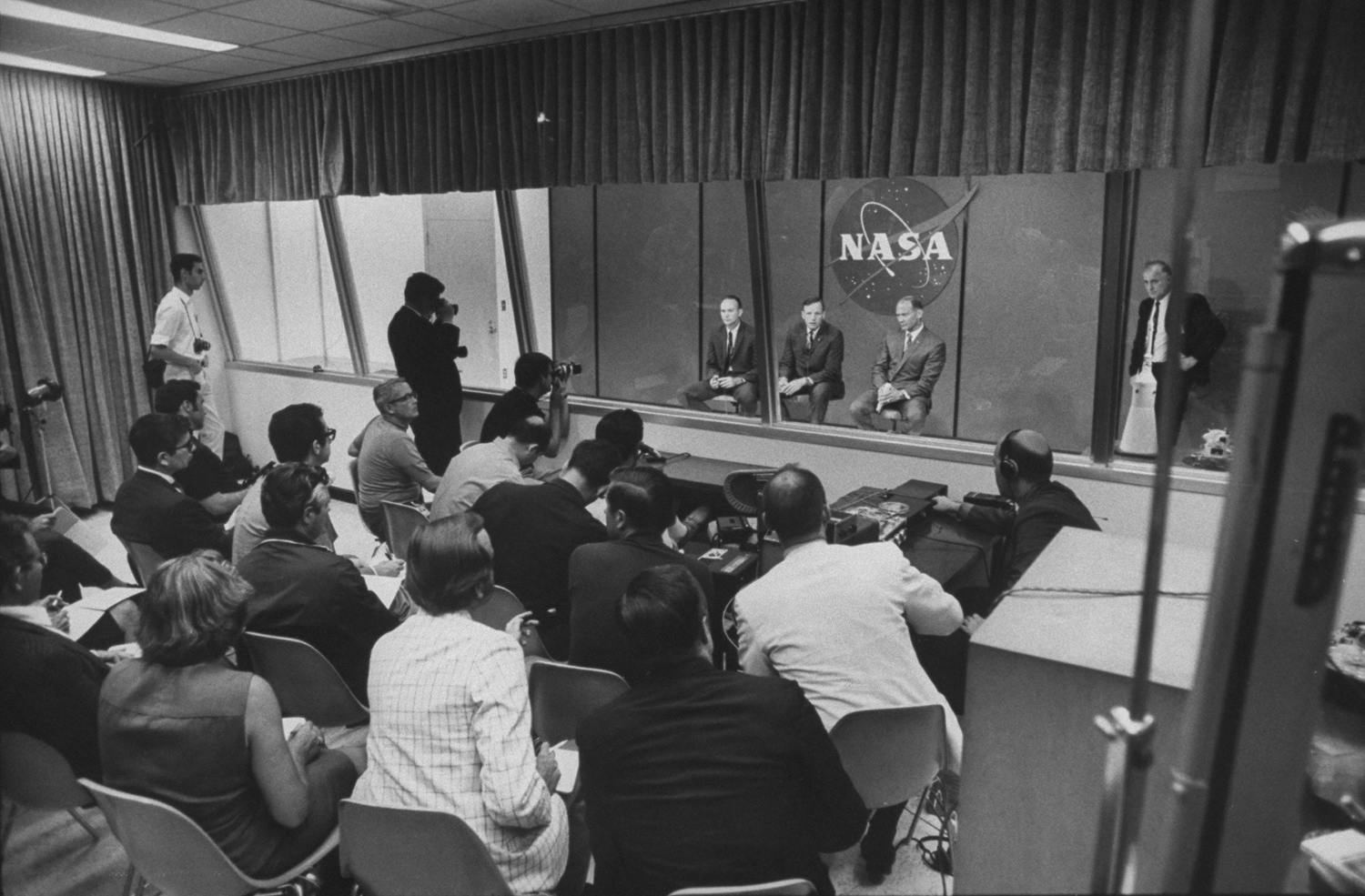 Collins, Armstrong and Aldrin inside a glass-enclosed cage to preserve their post-mission quarantine, July 1969.