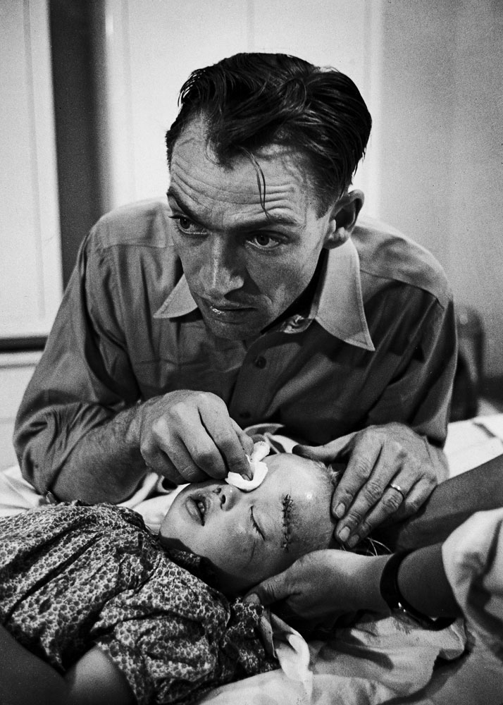 An intensely concerned Dr. Ernest Ceriani holds a bandage on the eye of a young girl whose head he has just stitched up after she was kicked by a horse, Colorado, 1948.