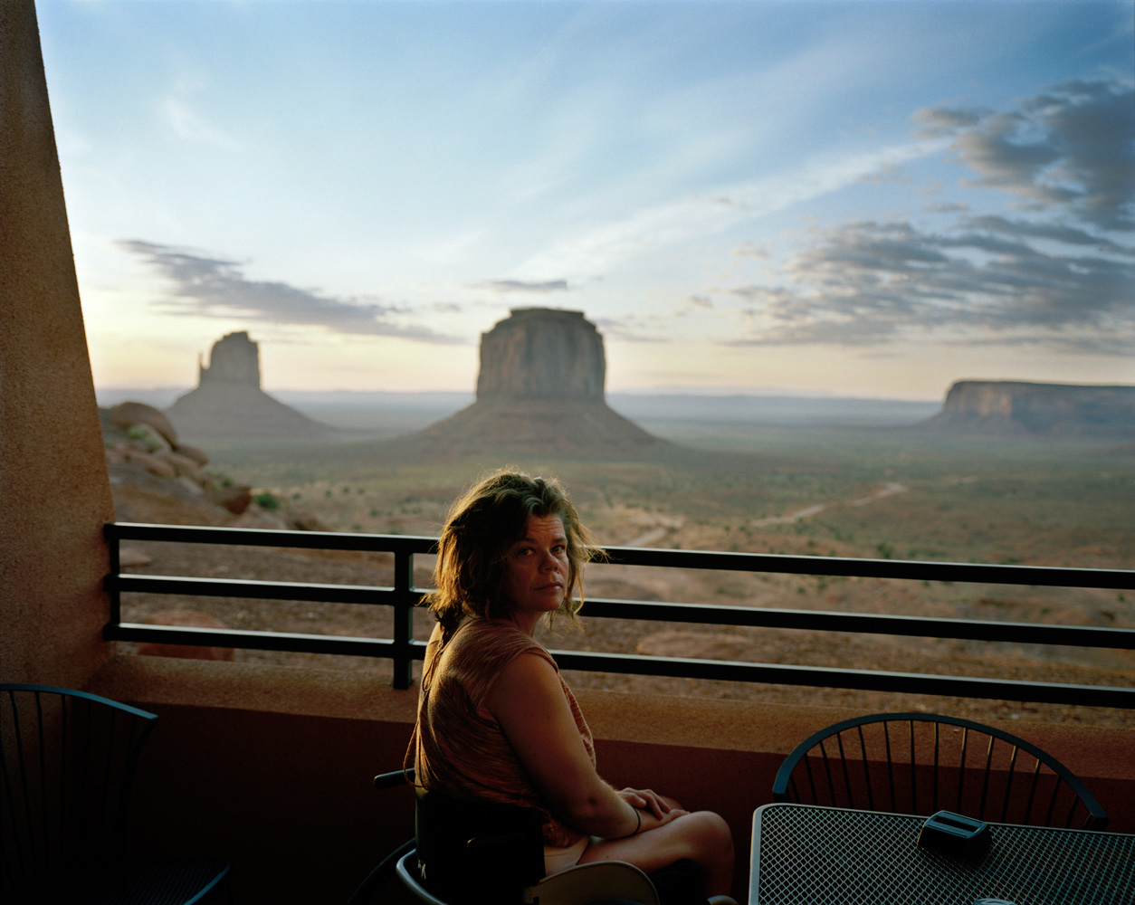 Nicole, Monument Valley, Utah, 2009 
                               I made this picture while on a road trip through the American West. Nicole and I had awoken at 5 a.m. to watch the sunrise over  The Mittens  and the photograph was made as an intuitive response to the light as it slowly emerged into the morning. It wasn’t until later, after the film was processed and I was going through the proofs, that I was able to see the potential in the photograph. The image evokes a sense of loss, both psychologically and metaphorically. Here, the majesty of the iconic American landscape is beyond reach — separated from us by a barrier — and only available as a distant view to look upon. The subject confronts us with this realization with her direct gaze. A sense of disconnection with the landscape is something not unfamiliar to Australians. White Australians live with the knowledge that we reside here in our country having dispossessed indigenous Australians from the land, and the process of reconciliation remains ongoing and unresolved.